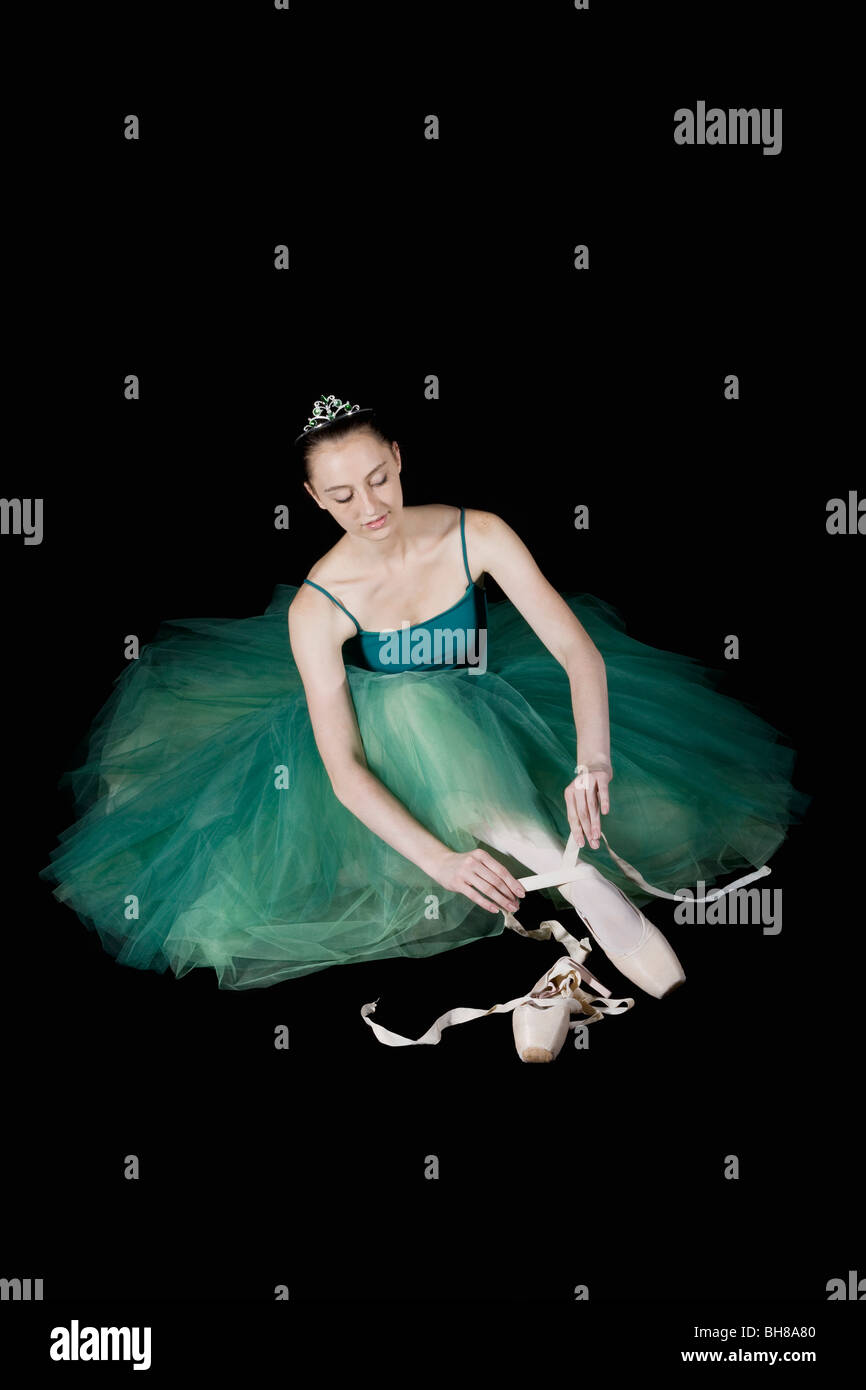 A ballet dancer wearing a costume tying her pointe shoe Stock Photo