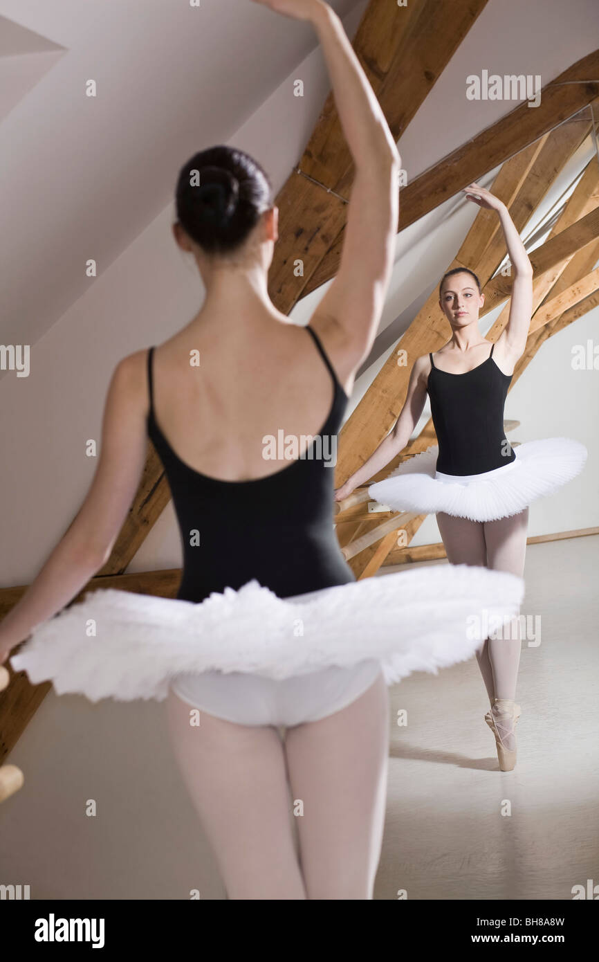 A ballet dancer on pointe with one arm raised in front of a mirror in a ballet studio Stock Photo