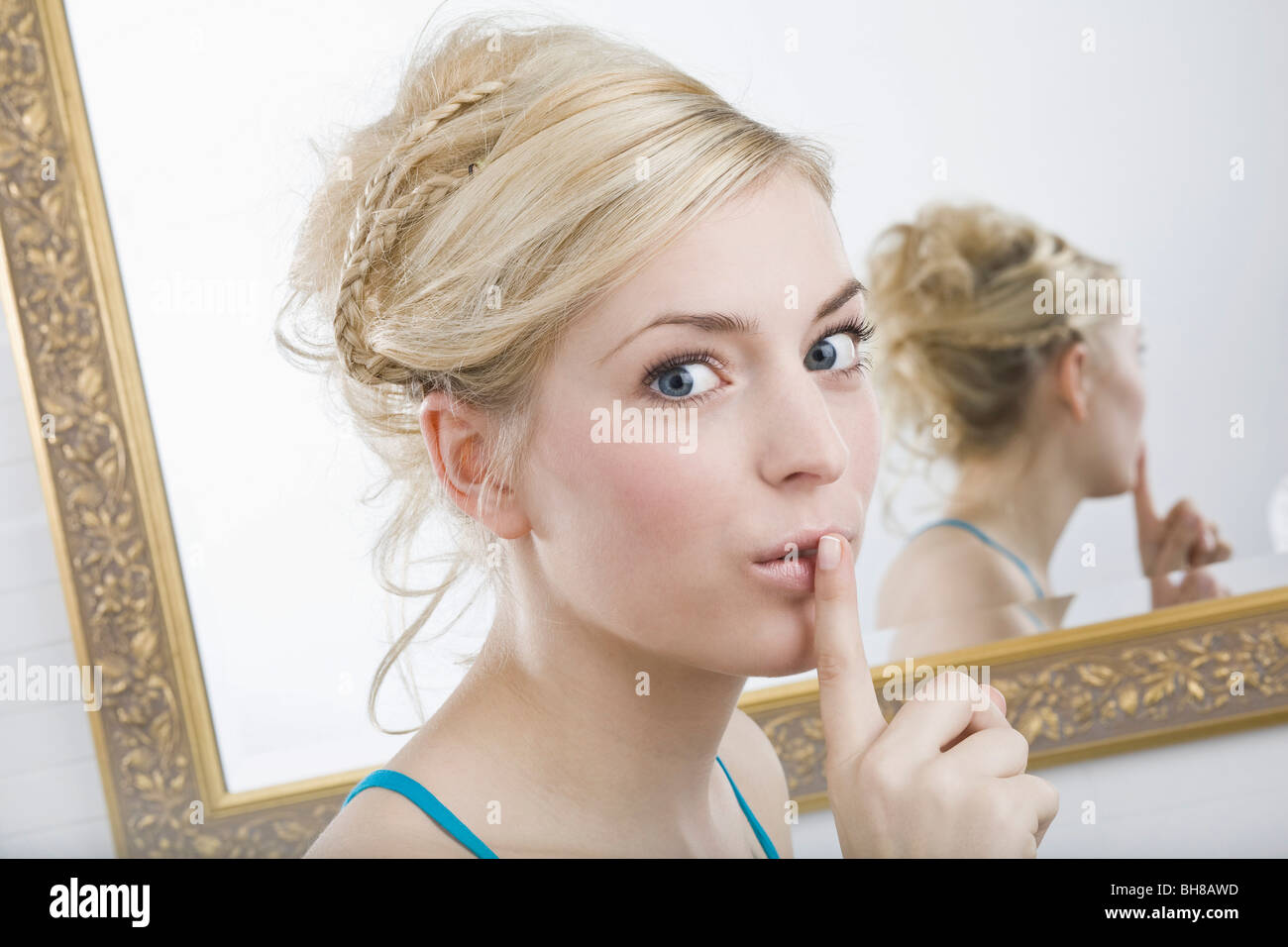 A woman with her finger to her lips in front of a mirror, looking at camera Stock Photo