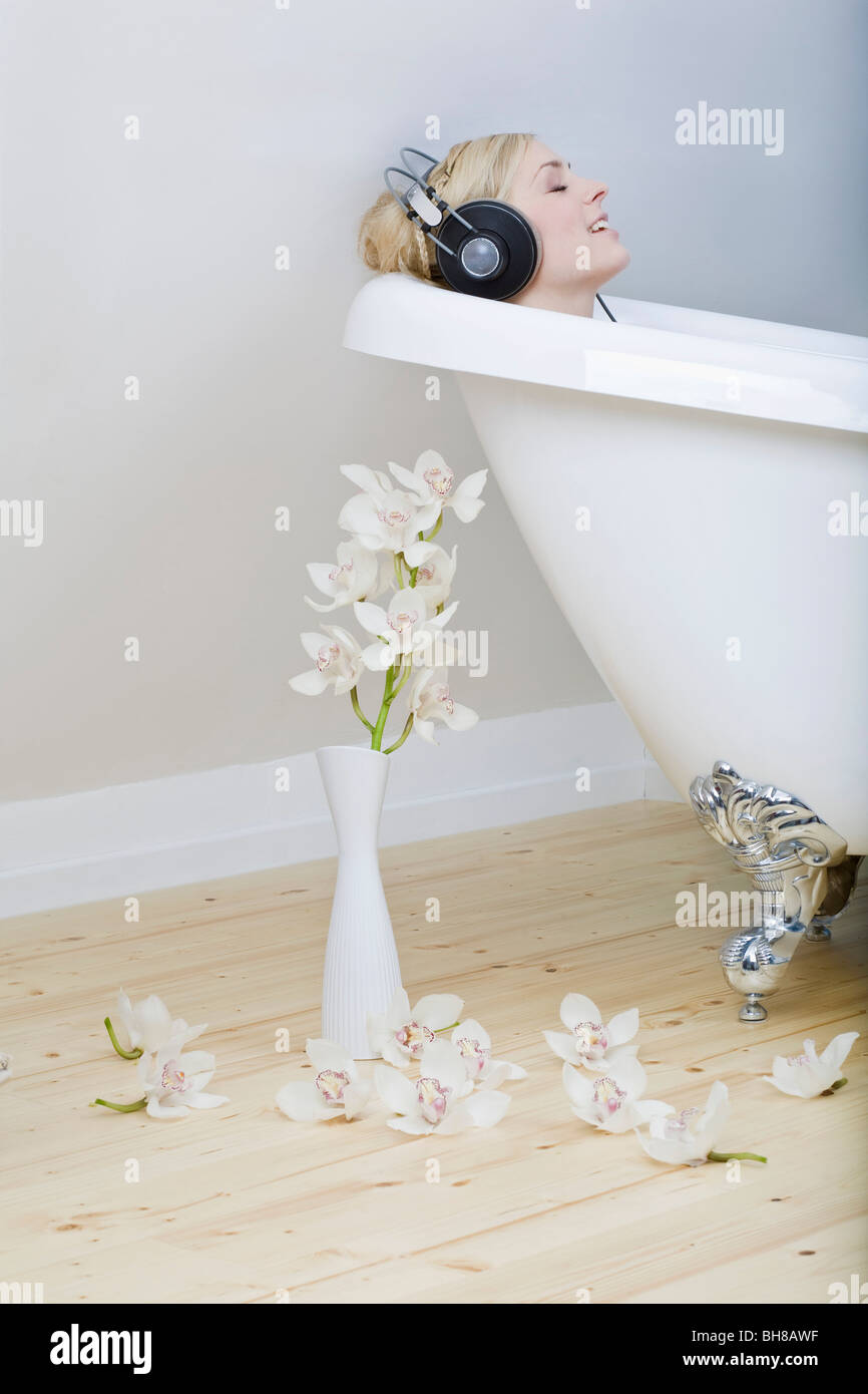 A woman enjoying a bath in a clawfoot tub, listening to headphones and singing along Stock Photo
