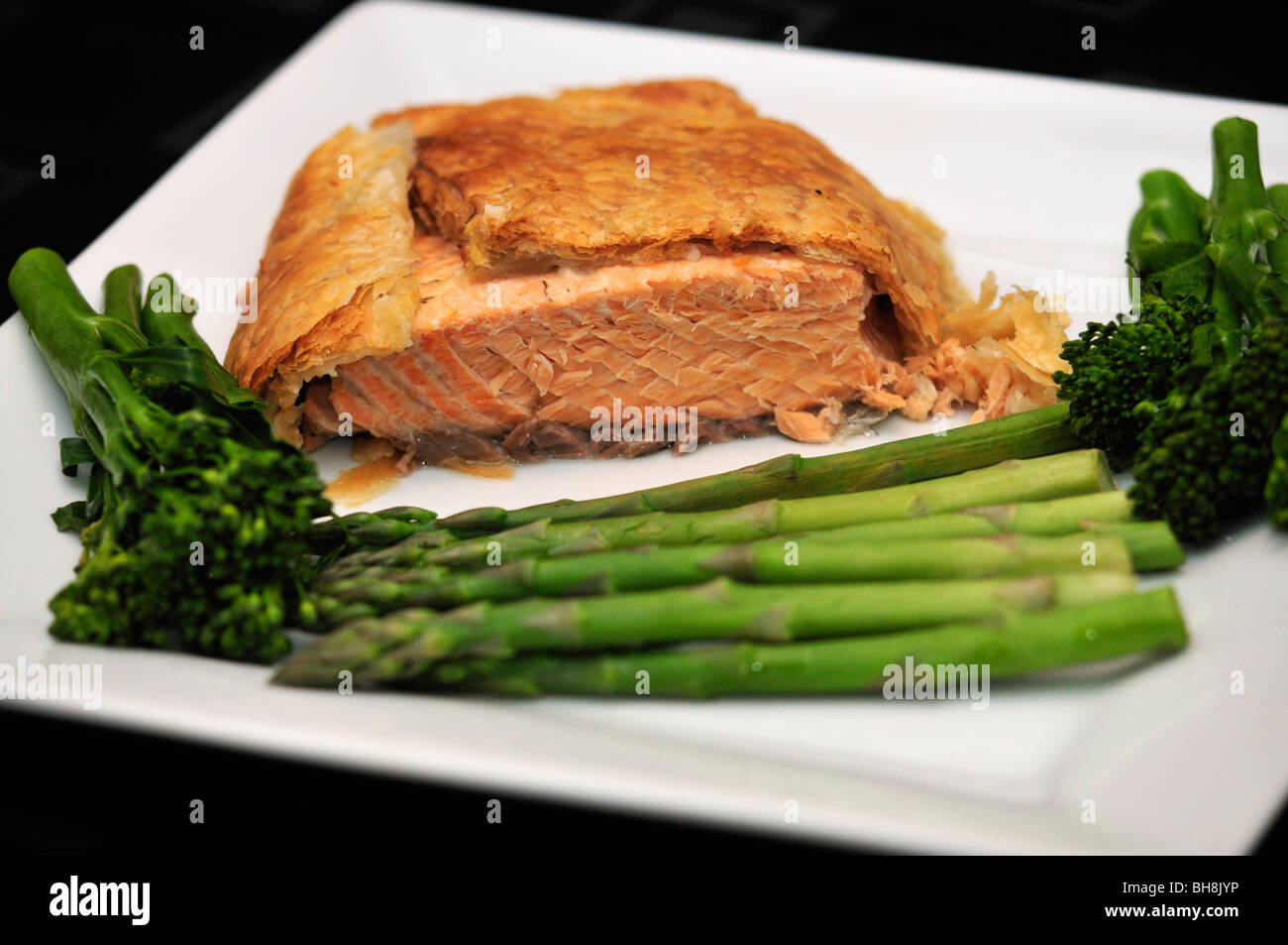 Salmon en croute with broccoli and asparagus on white serving plate on