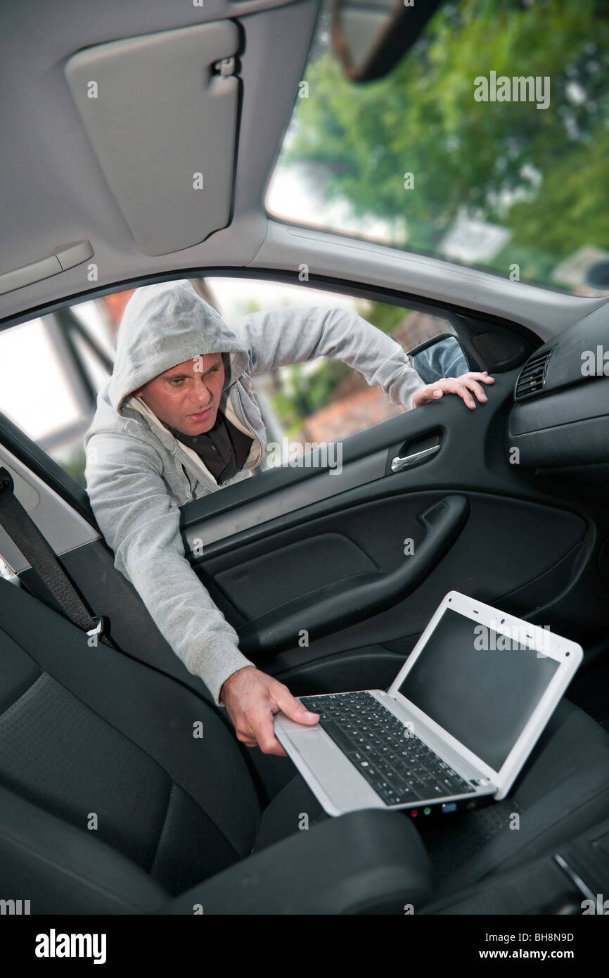 Car theft - a laptop being stolen through the window of an unoccupied car by a 'hoodie' Stock Photo