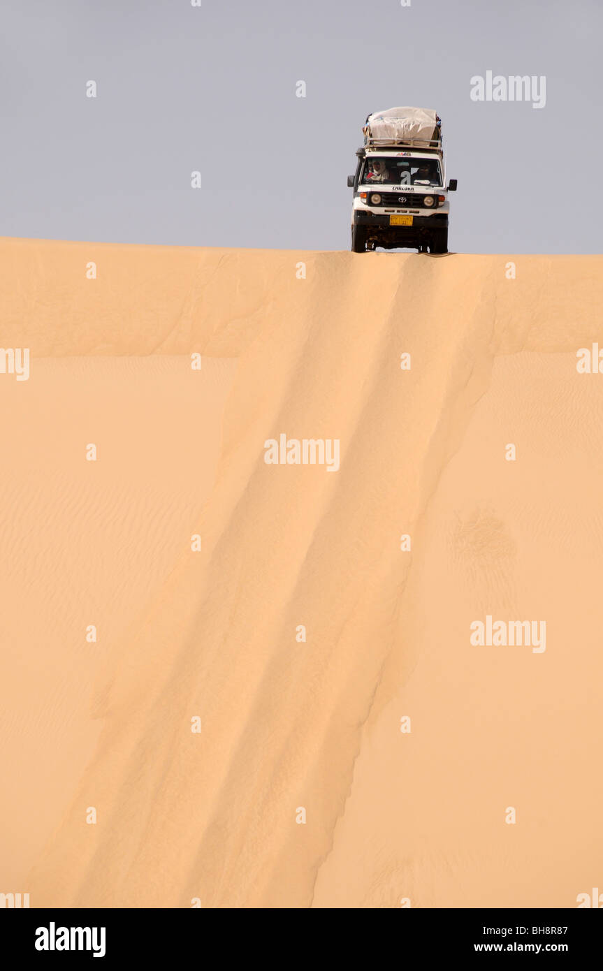 A desert safari land cruiser 4x4 jeep crests a giant sand dune in the Great Sand Sea of the Western Desert, Egyptian Sahara, Egypt. Stock Photo