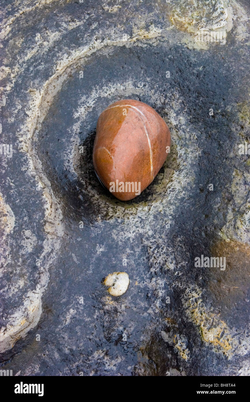 A glistening wet red pebble at the centre of a eroded hole in a beautiful striped rock Stock Photo