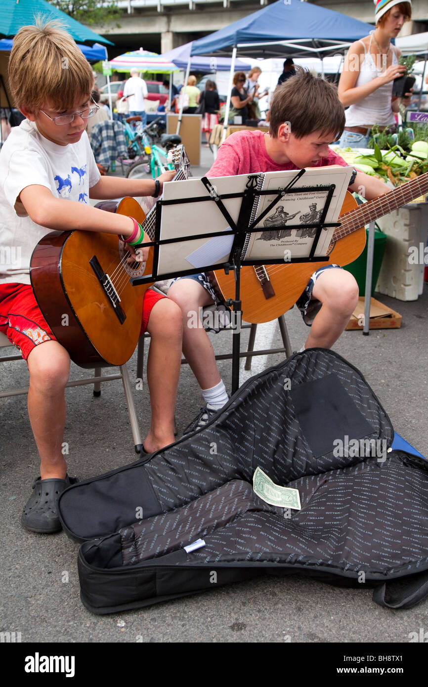 Two young boys performing,  playing guitars, concentrating hard and reading music from sheets on a music stand Stock Photo