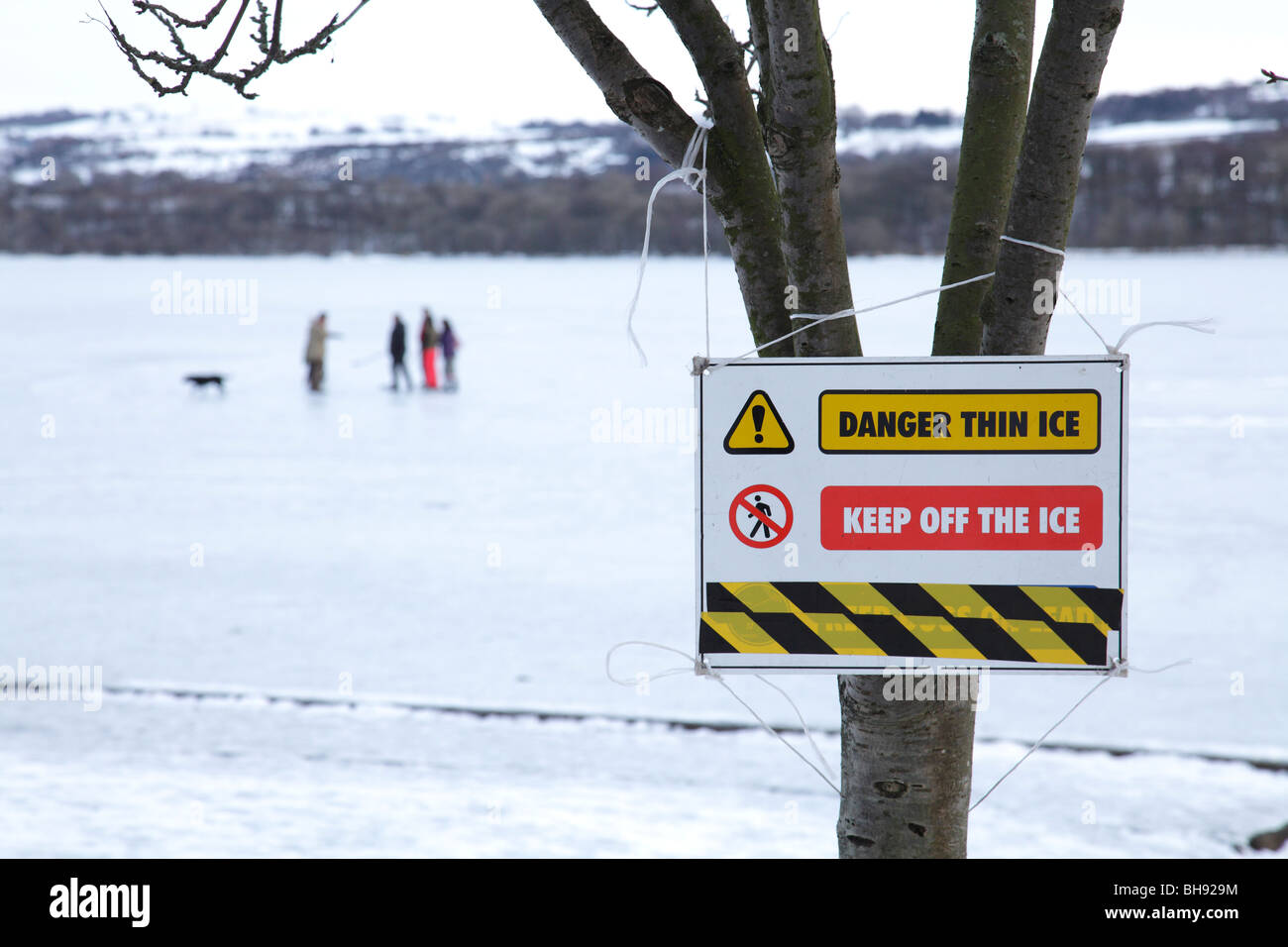 Thin Ice Warning sign beside a frozen Castle Semple Loch with people in winter, Clyde Muirshiel Regional Park, Lochwinnoch, Renfrewshire, Scotland, UK Stock Photo