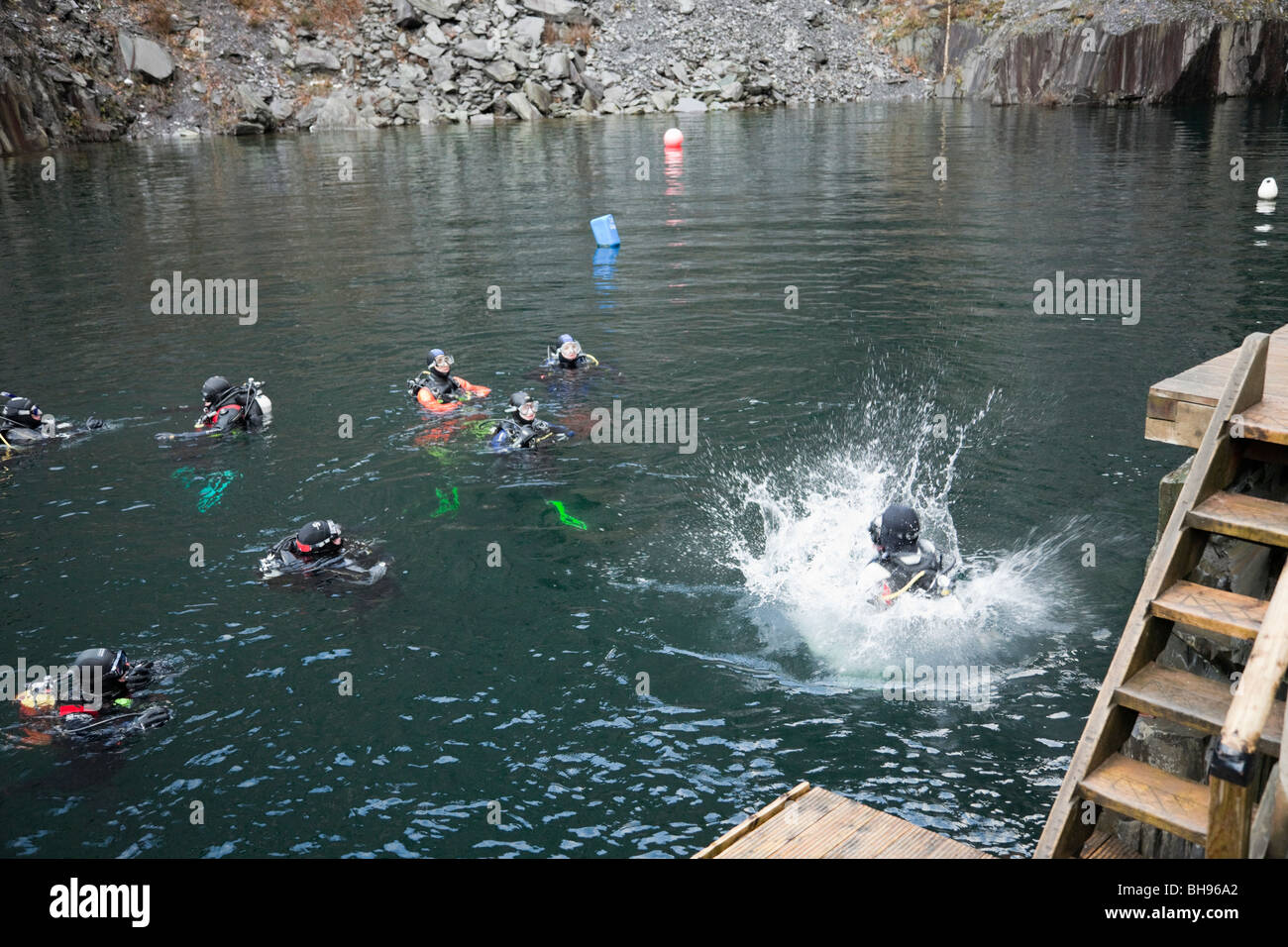 Divers training in flooded quarry with diver jumping in deep water at
