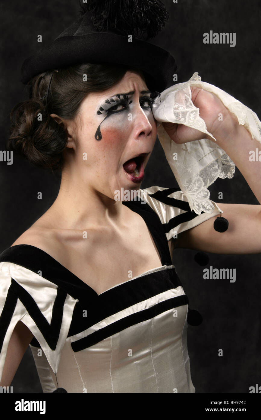 Young Woman Dressed in a Black and White Clown Outfit and Black Hat, Crying with a Handkerchief. Stock Photo