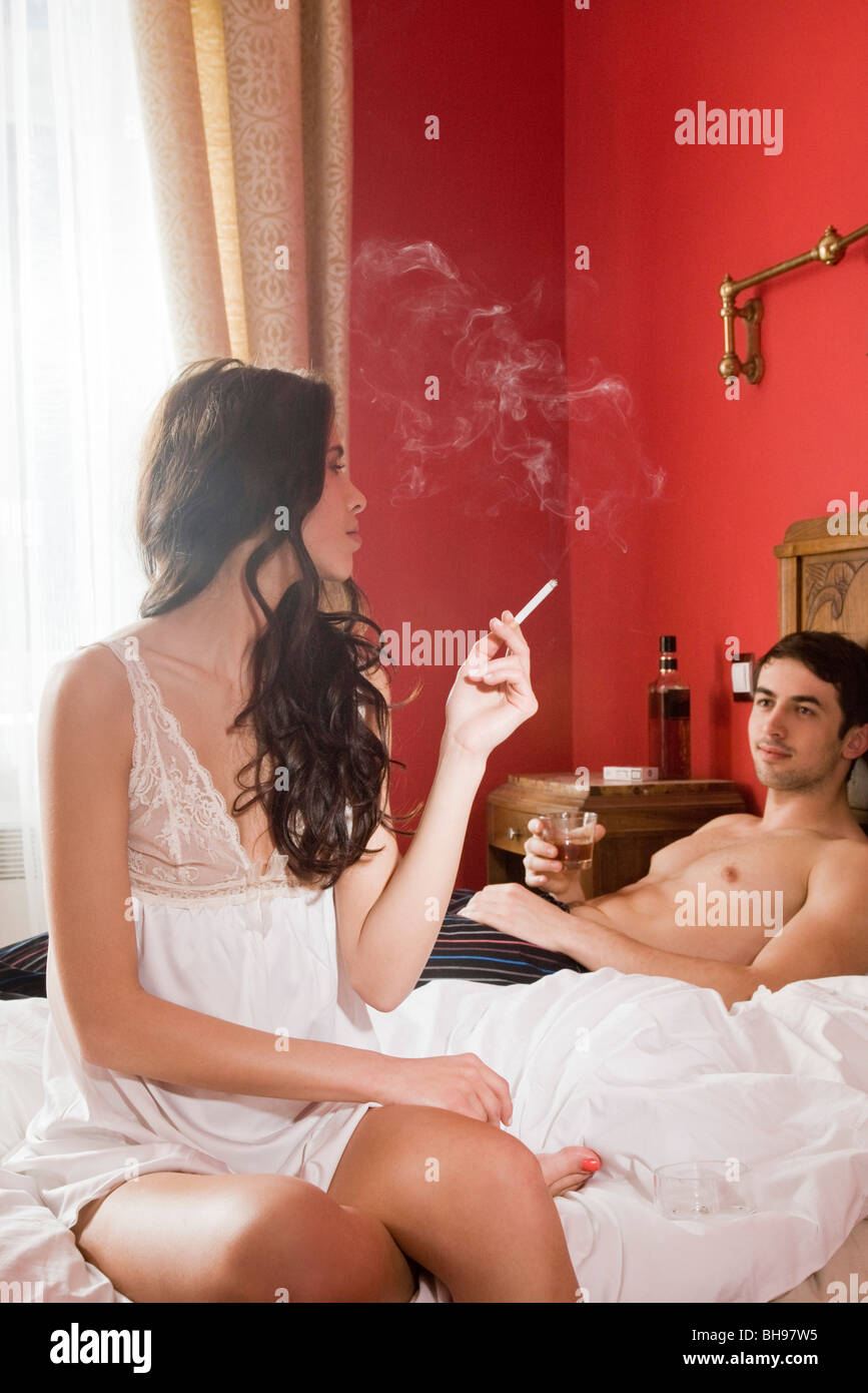 couple having drink and smoking cigarettes in bed Stock Photo