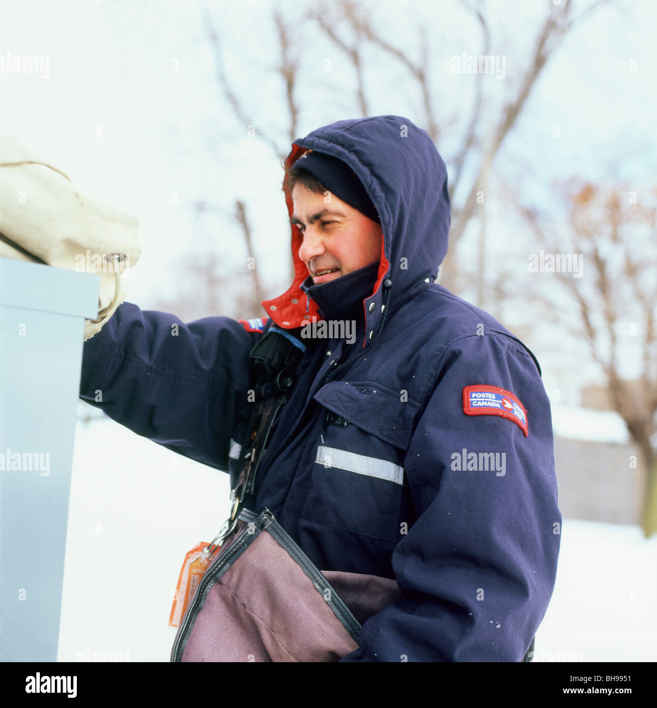 Canadian postman with postal worker bag at work outside outdoors in winter clothing delivering letters in the snow Ontario Canada  KATHY DEWITT Stock Photo