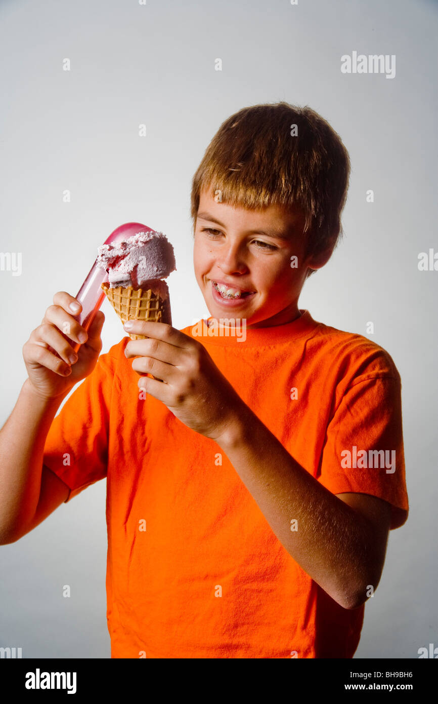 Smiling in anticipation, a happy ten year old boy places a scoop of ice cream in a waffle cone. Stock Photo