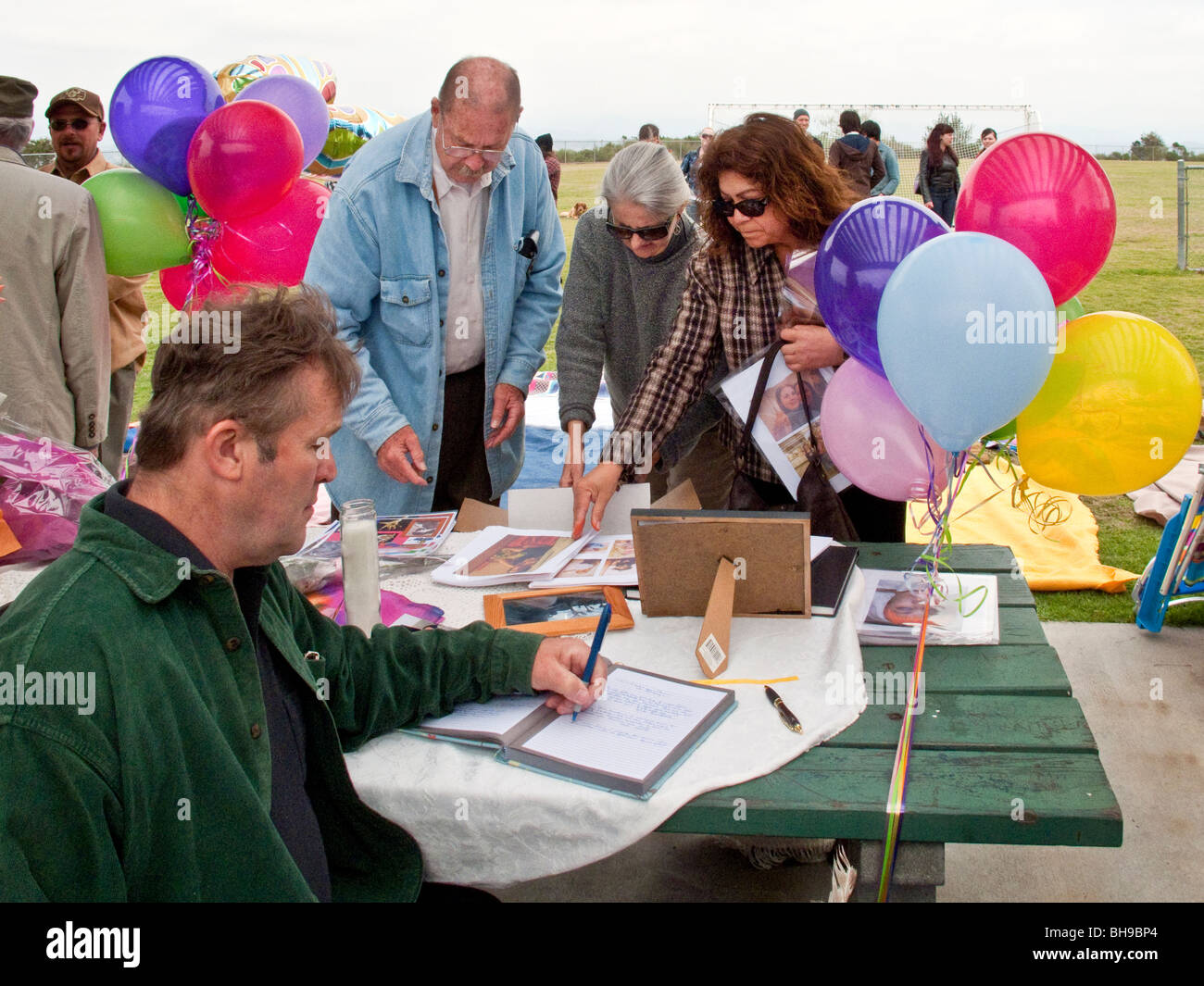 The father of a young adult suicide arranges photos of his late daughter at an outdoor memorial service at a public park. Stock Photo