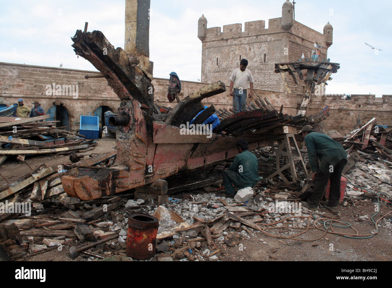 Scrap merchants work on the shipwreck in the port of Essaouira, protected by the city walls Stock Photo