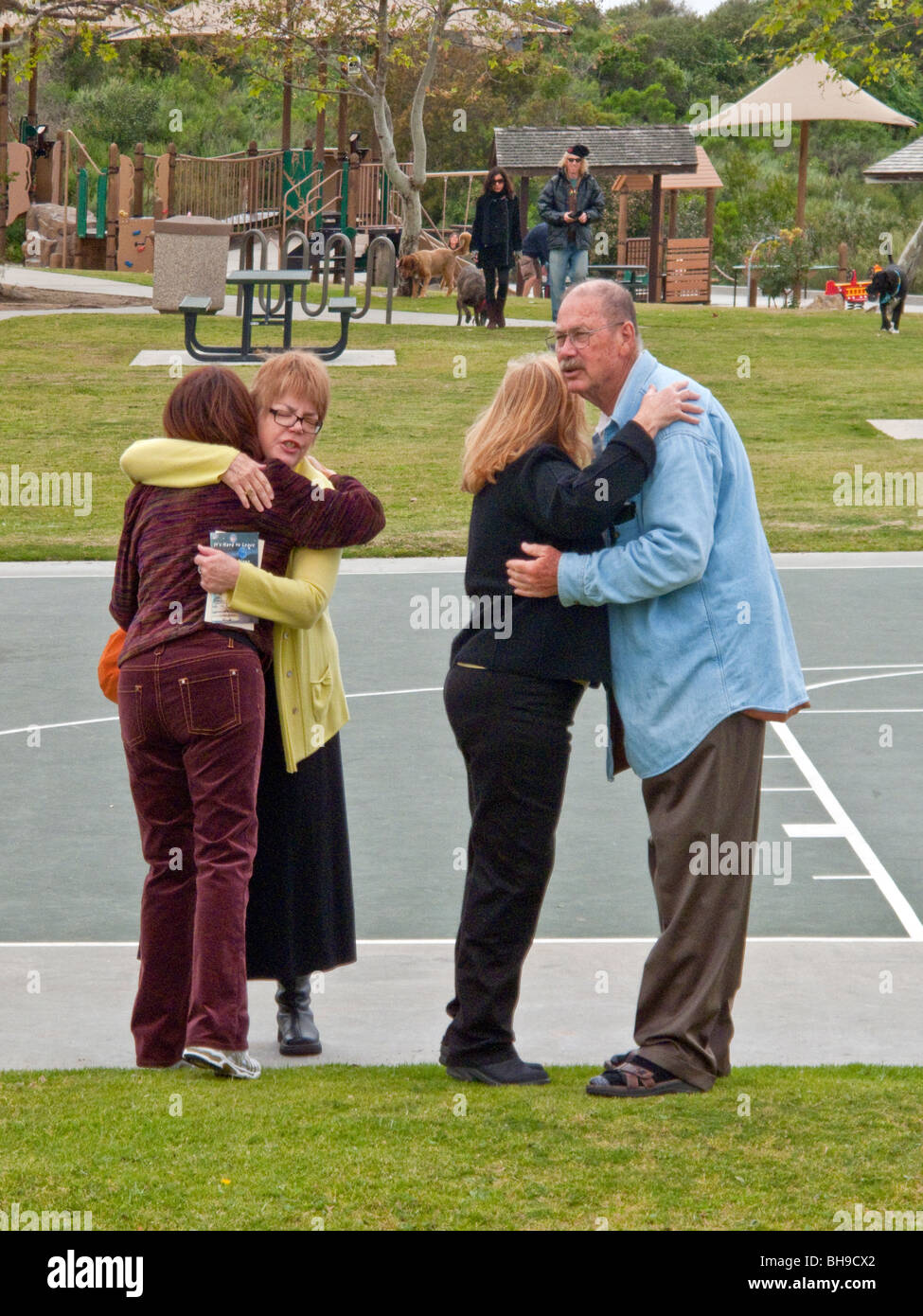 The parents of a young adult suicide are hugged by well-wishers at an outdoor memorial service in Laguna Beach, California. Stock Photo