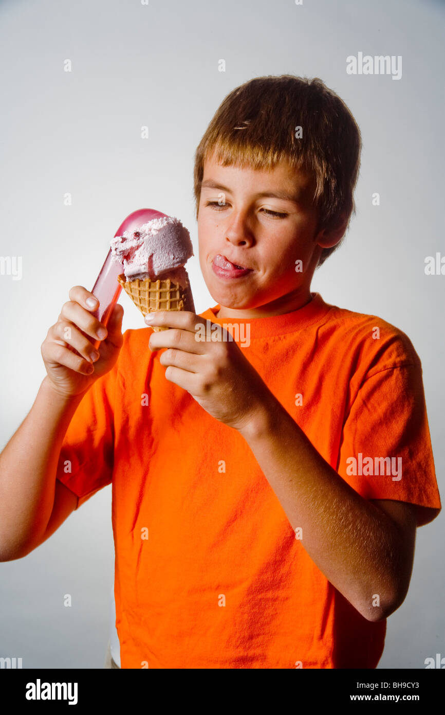 Licking his lips in anticipation, a happy ten year old boy places a scoop of ice cream in a waffle cone. Stock Photo
