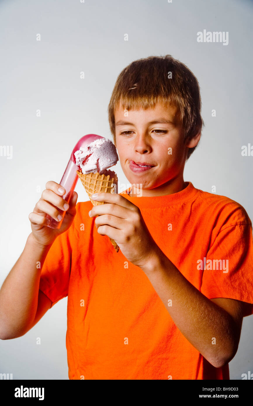 Licking his lips in anticipation, a happy ten year old boy places a scoop of ice cream in a waffle cone. Stock Photo