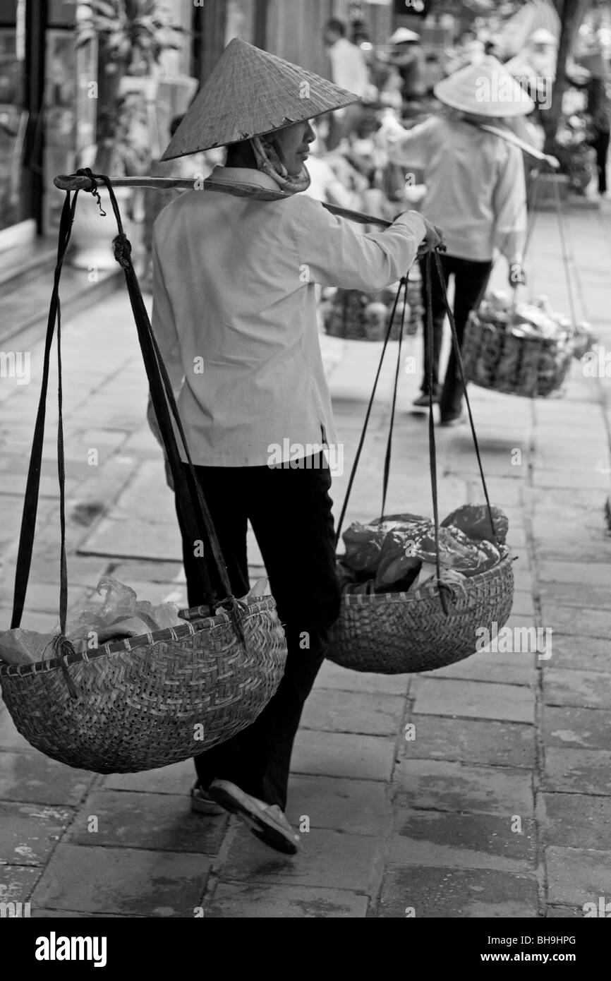 Vietnamese women with Asian style conical hats carrying baskets on the shoulders and selling their goods on the streets of Hanoi in North Vietnam. Stock Photo