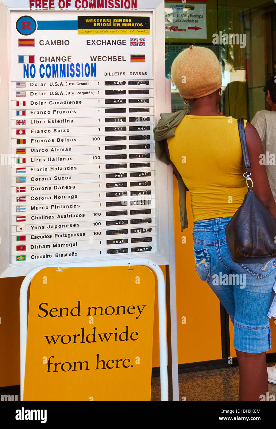 Woman leaning against international currency exchange rate board outside Western Union office in Fuengirola, Spain Stock Photo