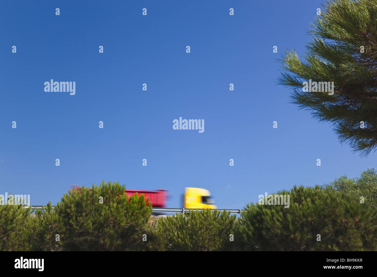 Red and yellow truck on highway under blue sky Stock Photo