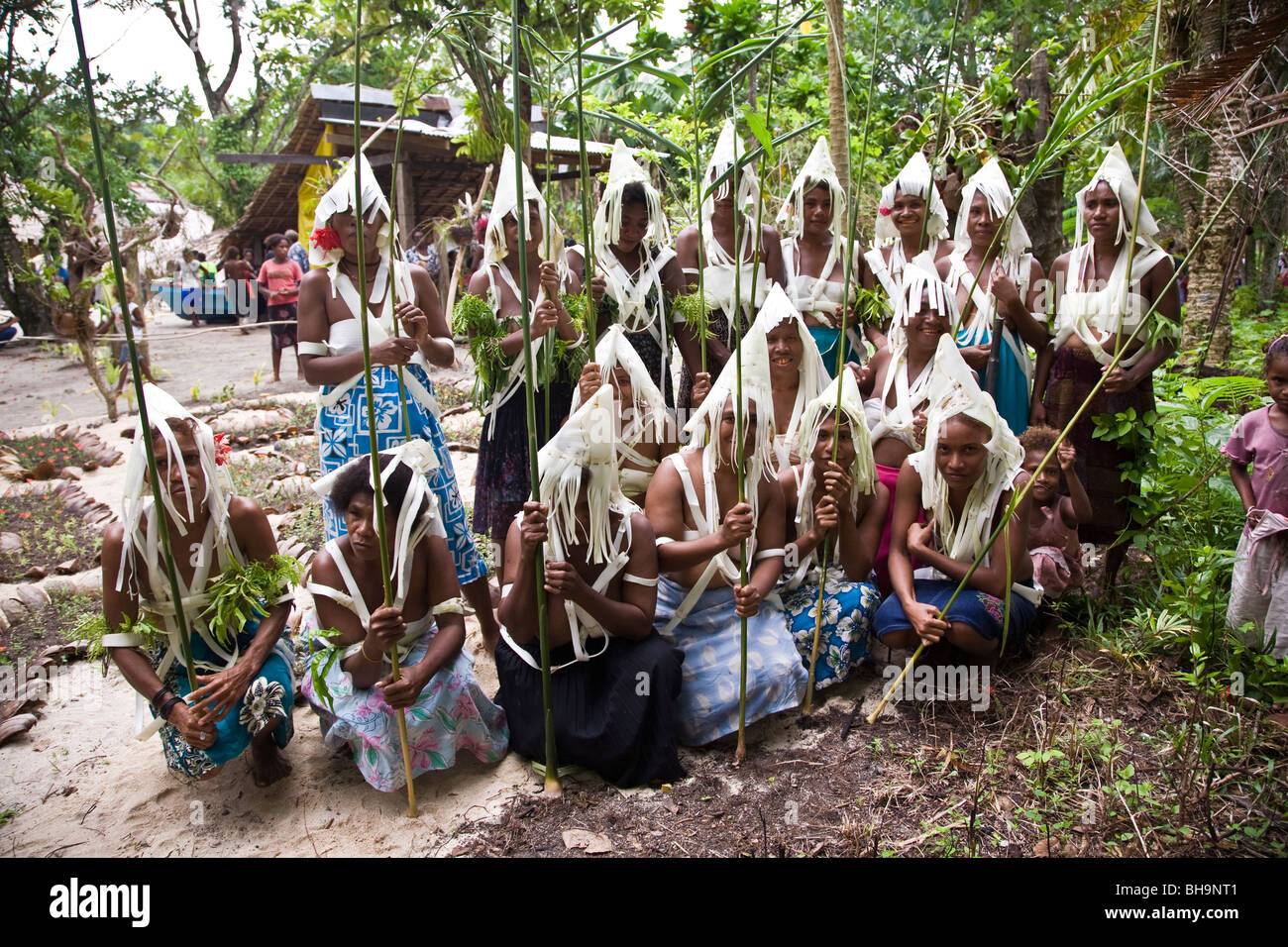 A group of Melanesian people in traditional white head dress holding spears made of plant poles Stock Photo