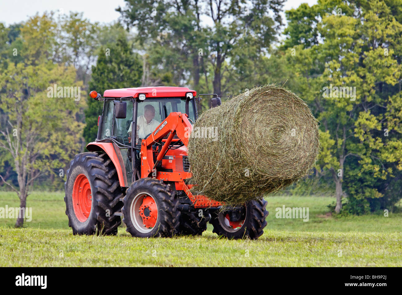 Man Moving Round Hay Bale with Kubota M9000 Tractor with LA1251 Loader on Farm in Oldham County, Kentucky Stock Photo