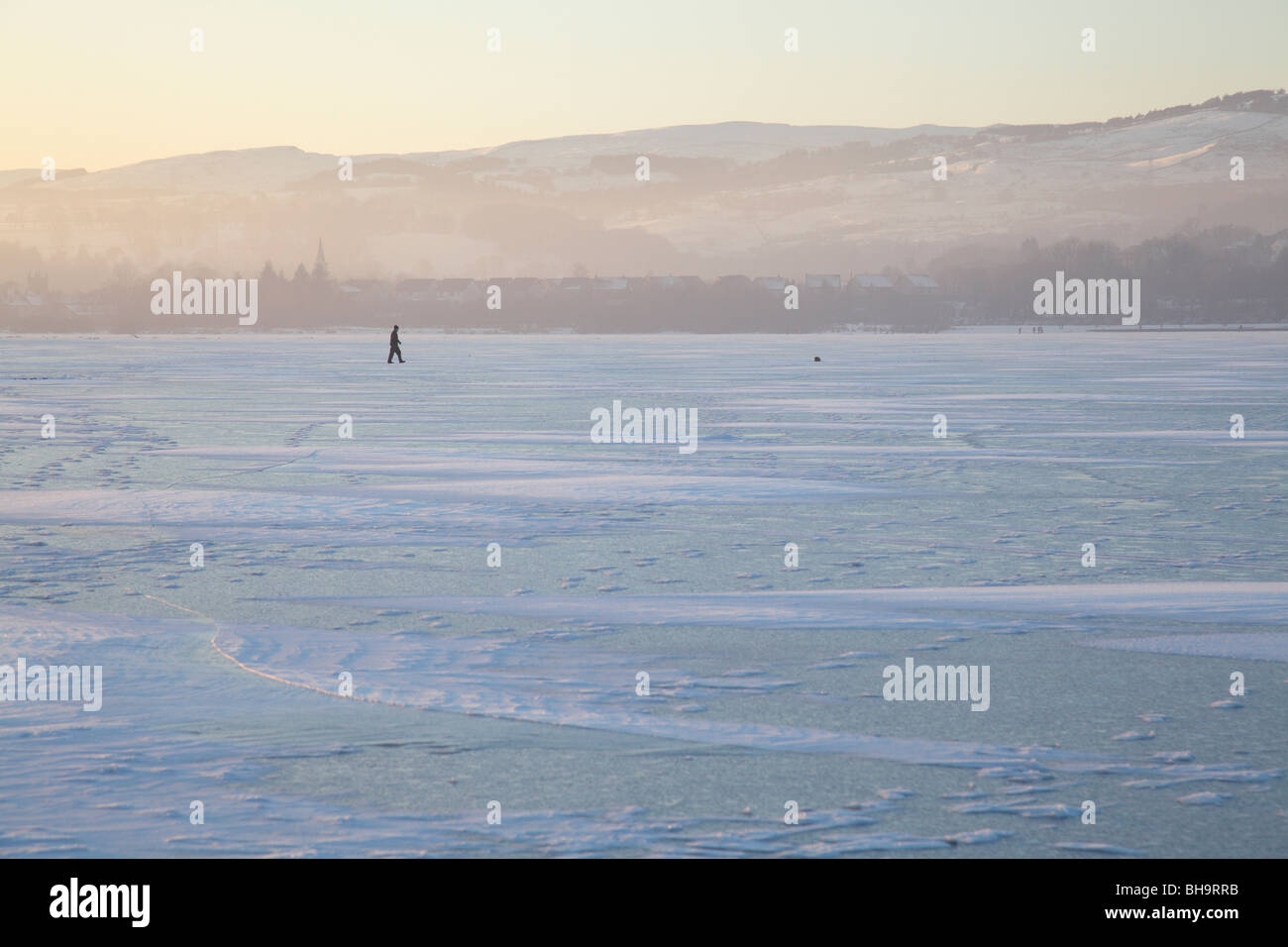 Man walking on a frozen Castle Semple Loch in winter, Clyde Muirshiel Regional Park, Lochwinnoch, Renfrewshire, Scotland, UK Stock Photo
