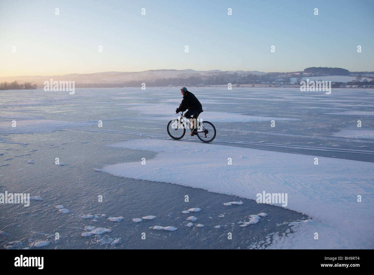 Man cycling in winter on a frozen Castle Semple Loch, Lochwinnoch, Renfrewshire, Scotland, UK Stock Photo