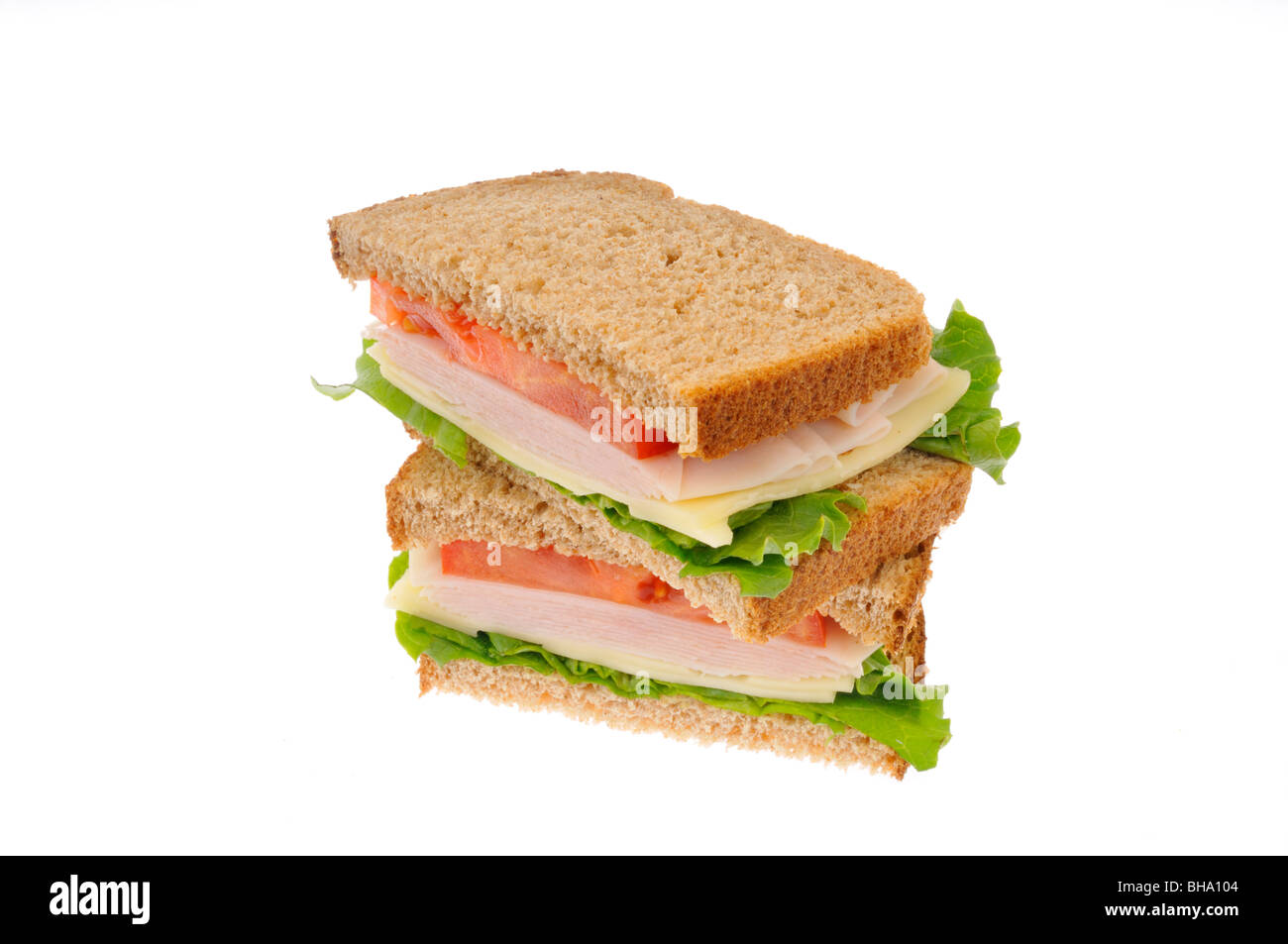 2 halves of turkey and cheese sandwich with lettuce and tomato on wholemeal bread stacked on white background. Cut out Stock Photo