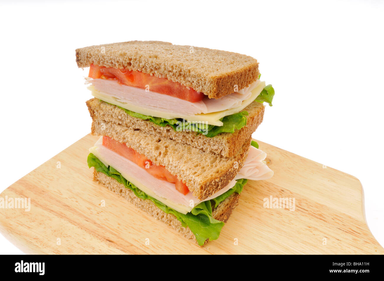 2 halves of turkey and cheese sandwich with lettuce and tomato on whole wheat bread stacked on chopping board. Stock Photo