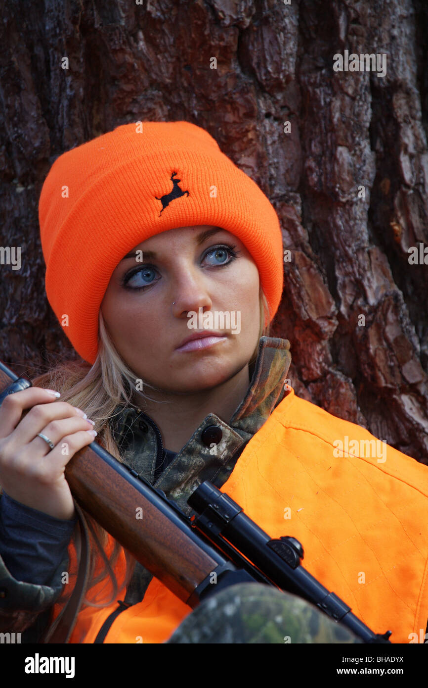 CLOSE UP YOUNG WOMAN 21 Y.O. FEMALE DEER HUNTER SITTING AGAINST TREE IN FOREST LOOKING FOR DEER
