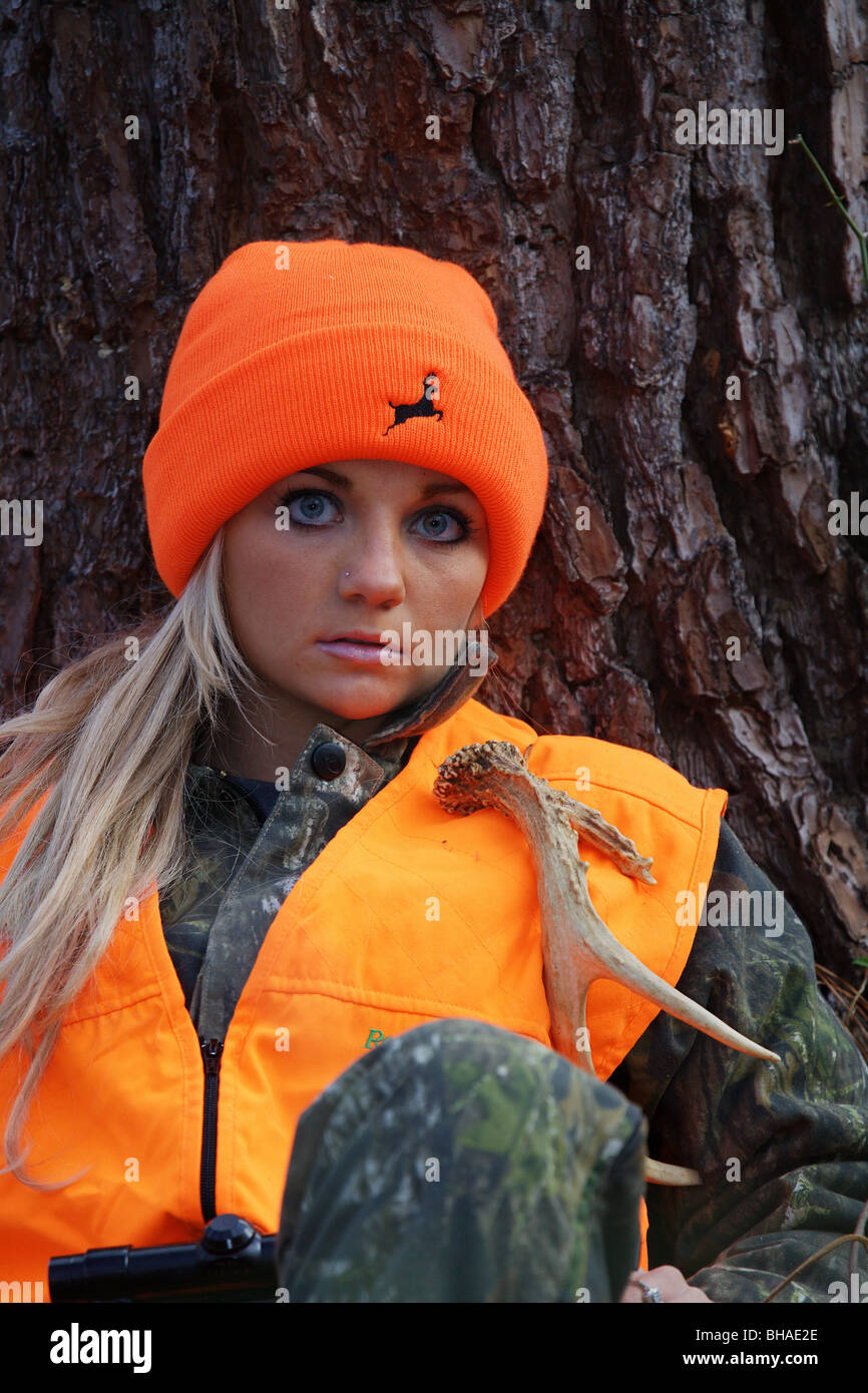 CLOSE UP YOUNG WOMAN 21 YO FEMALE DEER HUNTER SITTING AGAINST TREE IN FOREST LOOKING FOR DEER