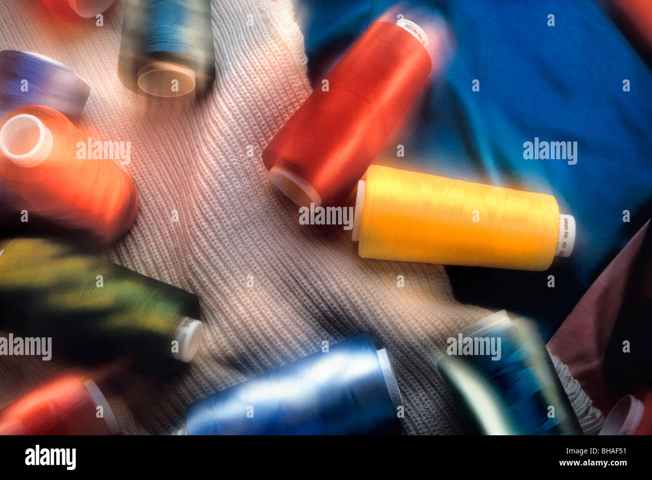 spools of thread lay on types of fabric in a garment industry still-life. Stock Photo