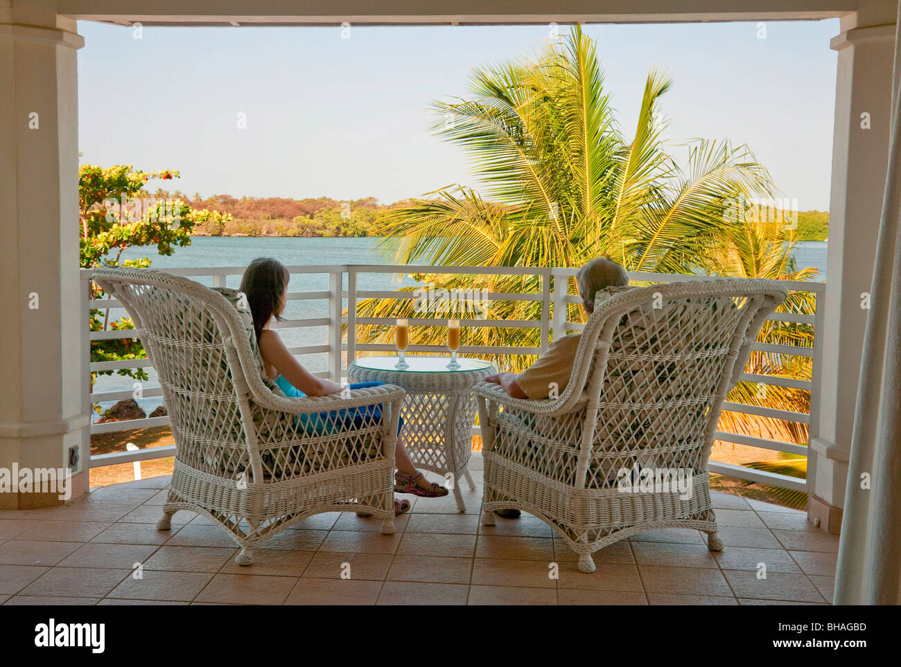 Couple sit and watch early morning sunrise from a balcony  over the Caribbean coast. Stock Photo