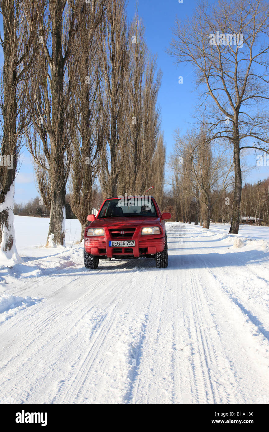 red Suzuki Jeep on snow covered alley road in winter landscape . Photo by Willy Matheisl Stock Photo