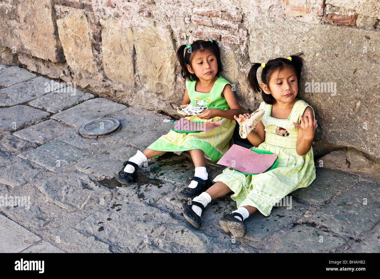 pretty little Mexican twin girls wear similar expressions as they sit