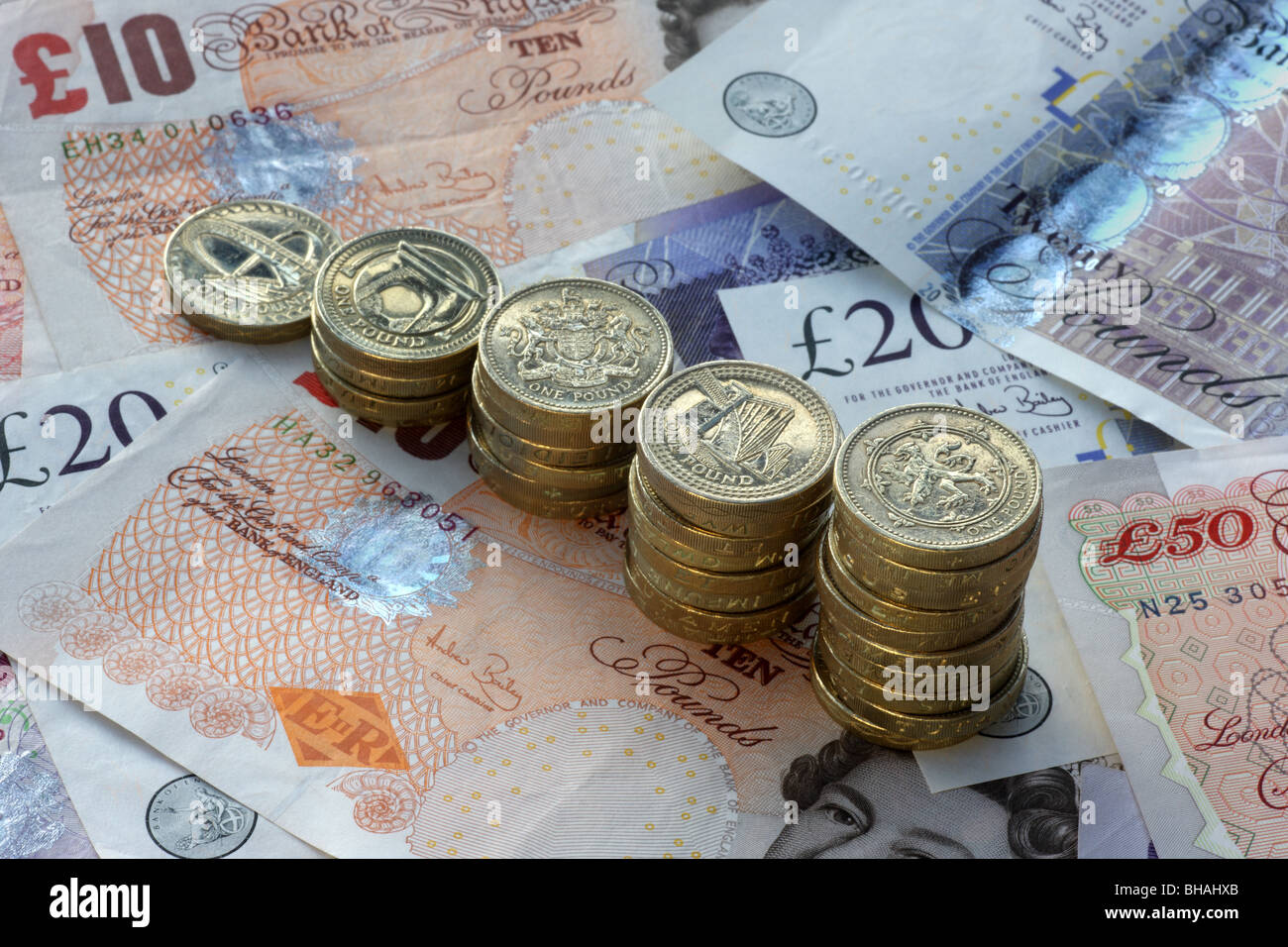 Five piles of one pound coins in increasing height on a background of fifty, twenty and ten pound notes. Stock Photo