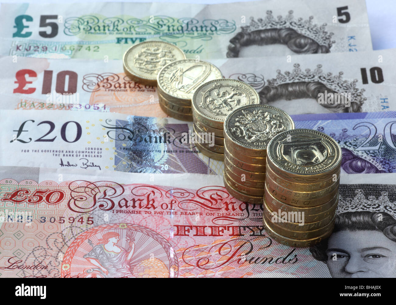 Five stacks of one pound coins in increasing size from one pound to nine pound coins. Five, ten, twenty pounds in background. Stock Photo