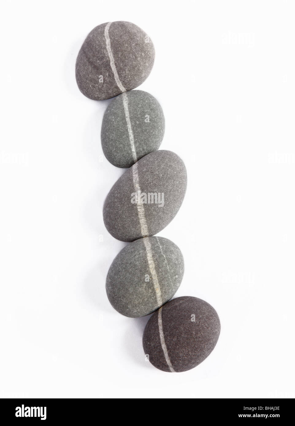 Five granite pebbles, each with one quartz vein, lined up so that the quartz veins create one continuous line. Stock Photo