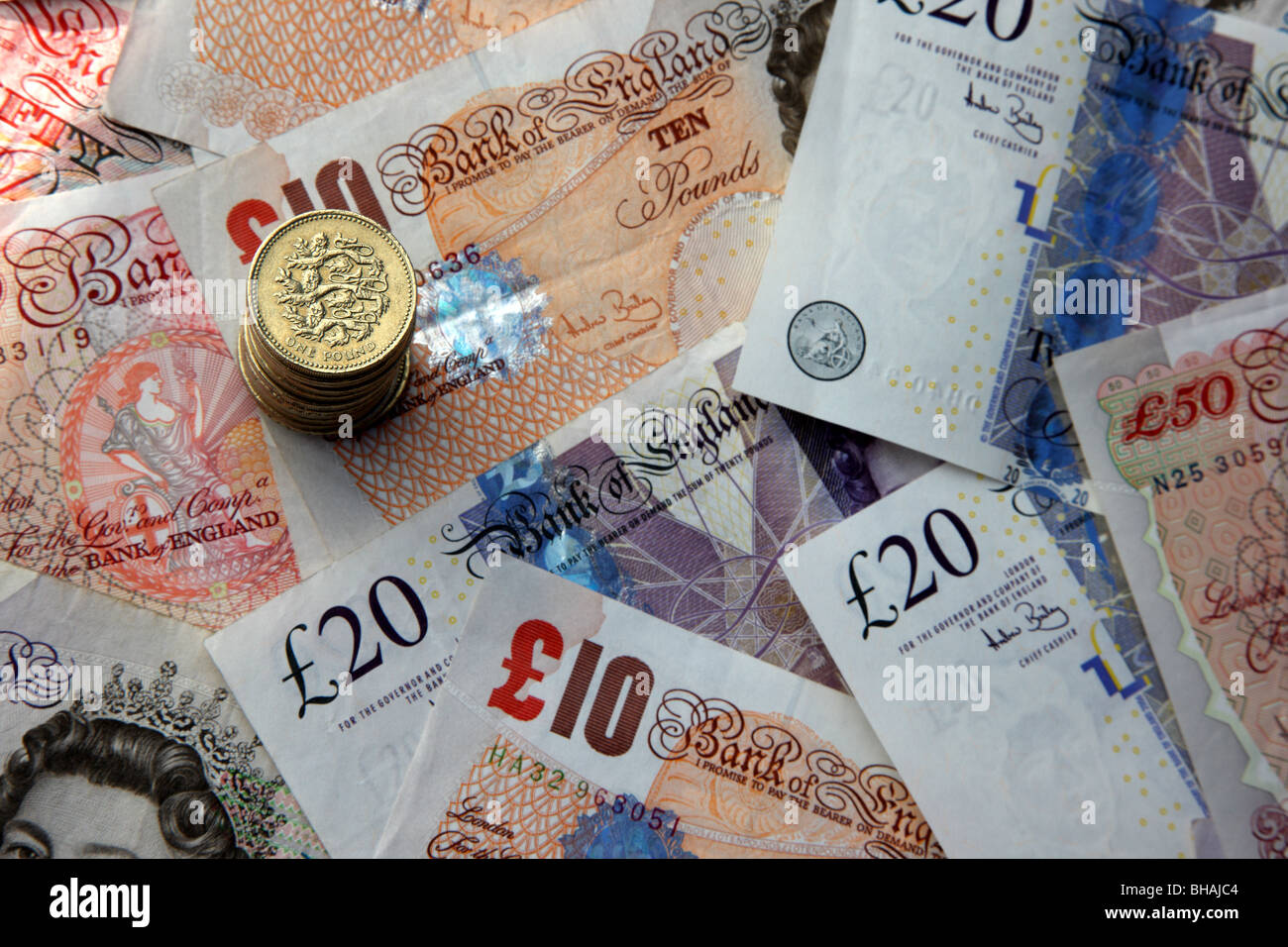 Stack of one pound coins on background of fifty, twenty and ten pound notes. Stock Photo