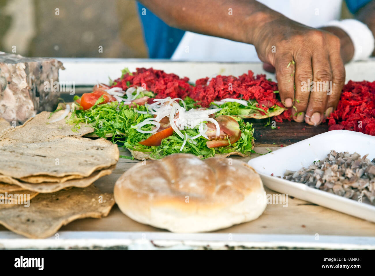 tempting tostadas being assembled by a sidewalk vendor on small portable cart partly enclosed by plexiglass Oaxaca City Stock Photo