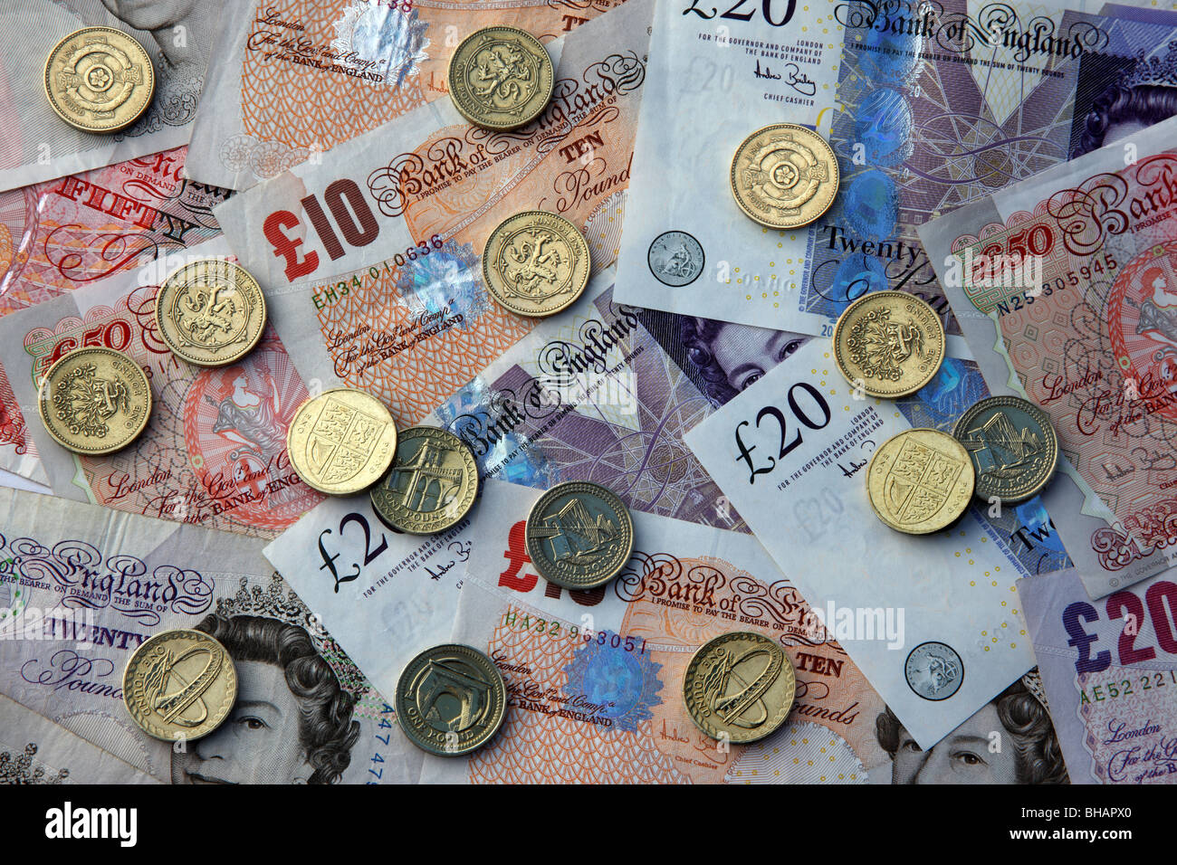 One pound coins scattered on bank notes, fifty, twenty and ten pound notes. Stock Photo