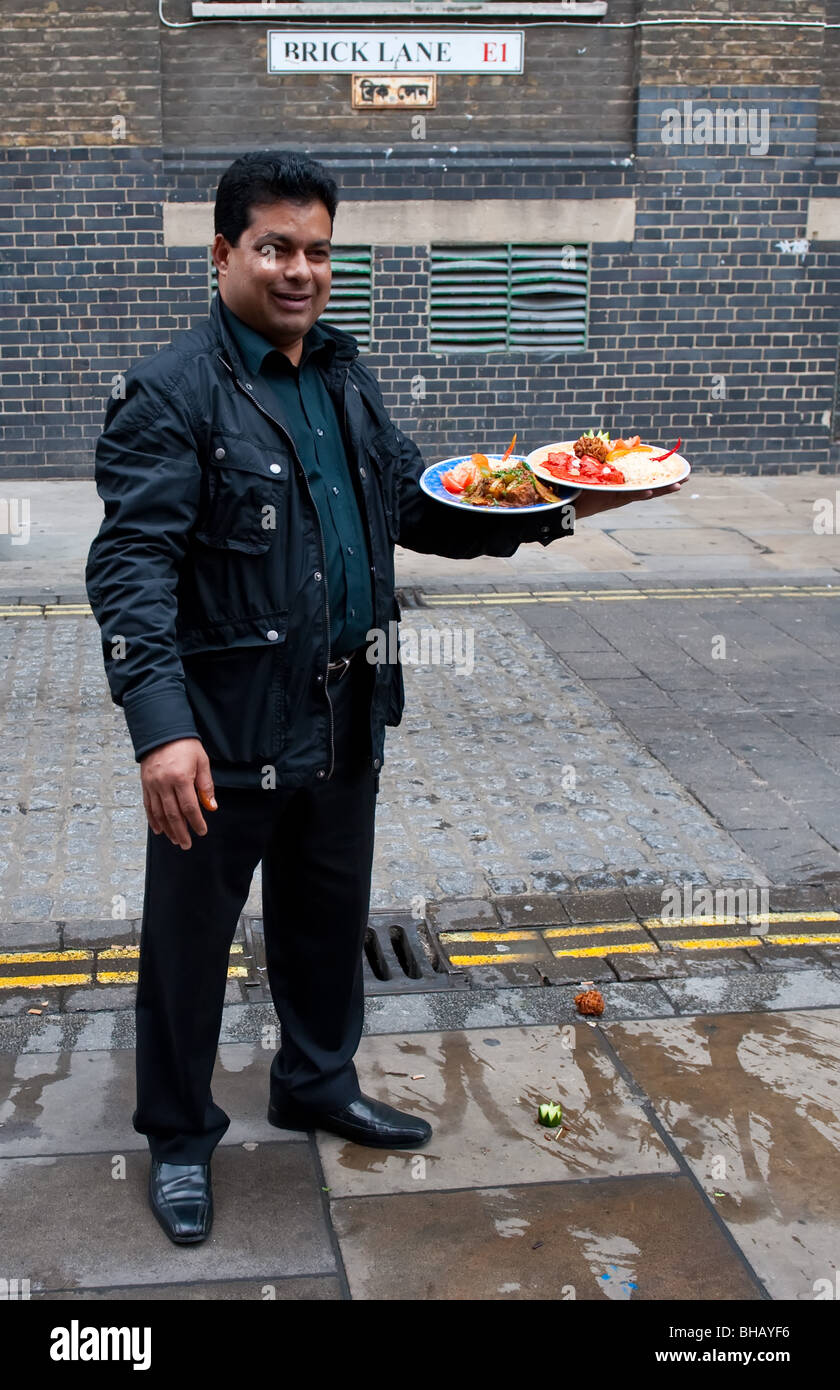A restaurant owner presenting two curries in Brick Lane, London Stock Photo