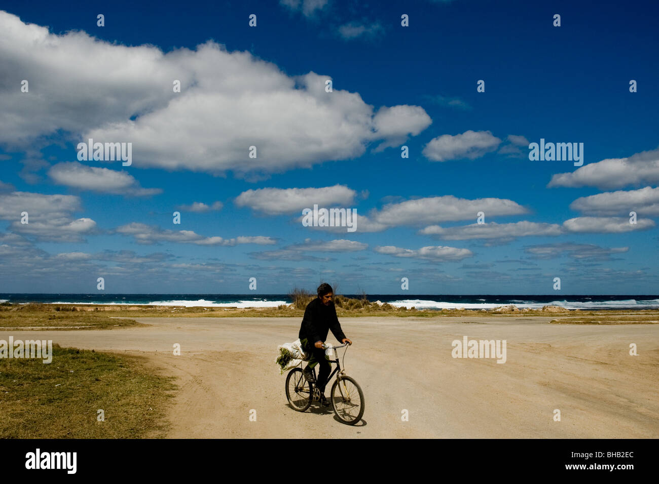 A Cuban man riding a bicycle on the road along the sea, carrying vegetables from his garden to his home in the Havana, Cuba. Stock Photo