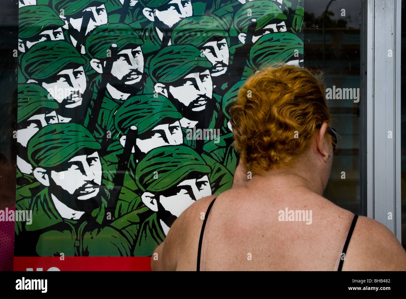 A Cuban woman looking through a shop window covered by the Fidel Castro's propaganda poster in Santiago de Cuba, Cuba. Stock Photo