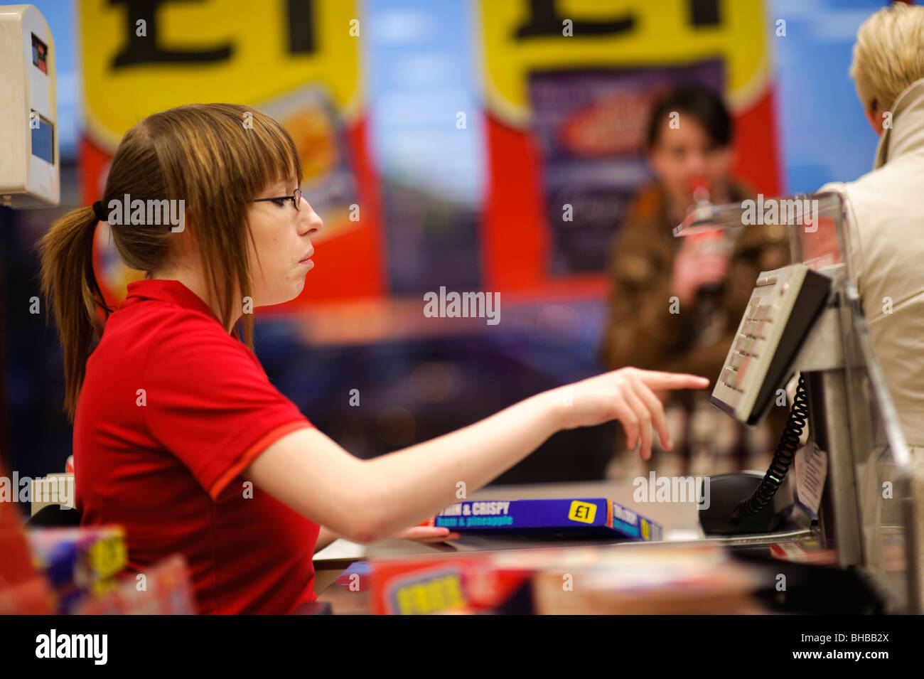 a Young girl woman cashier working at Iceland frozen food supermarket checkout till, UK Stock Photo