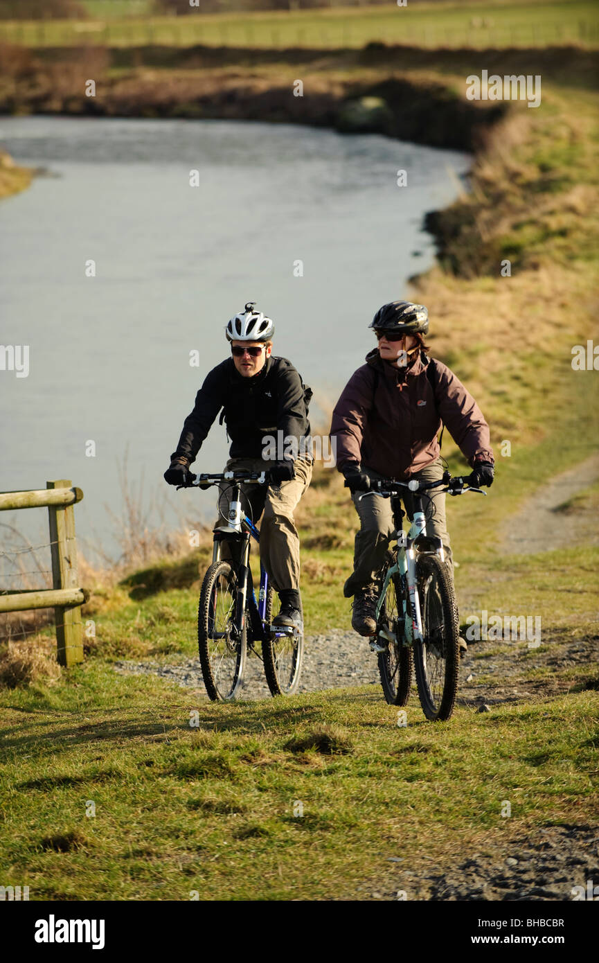 Two people cycling in the countryside along the Ystwyth river, Aberystwyth Wales UK Stock Photo