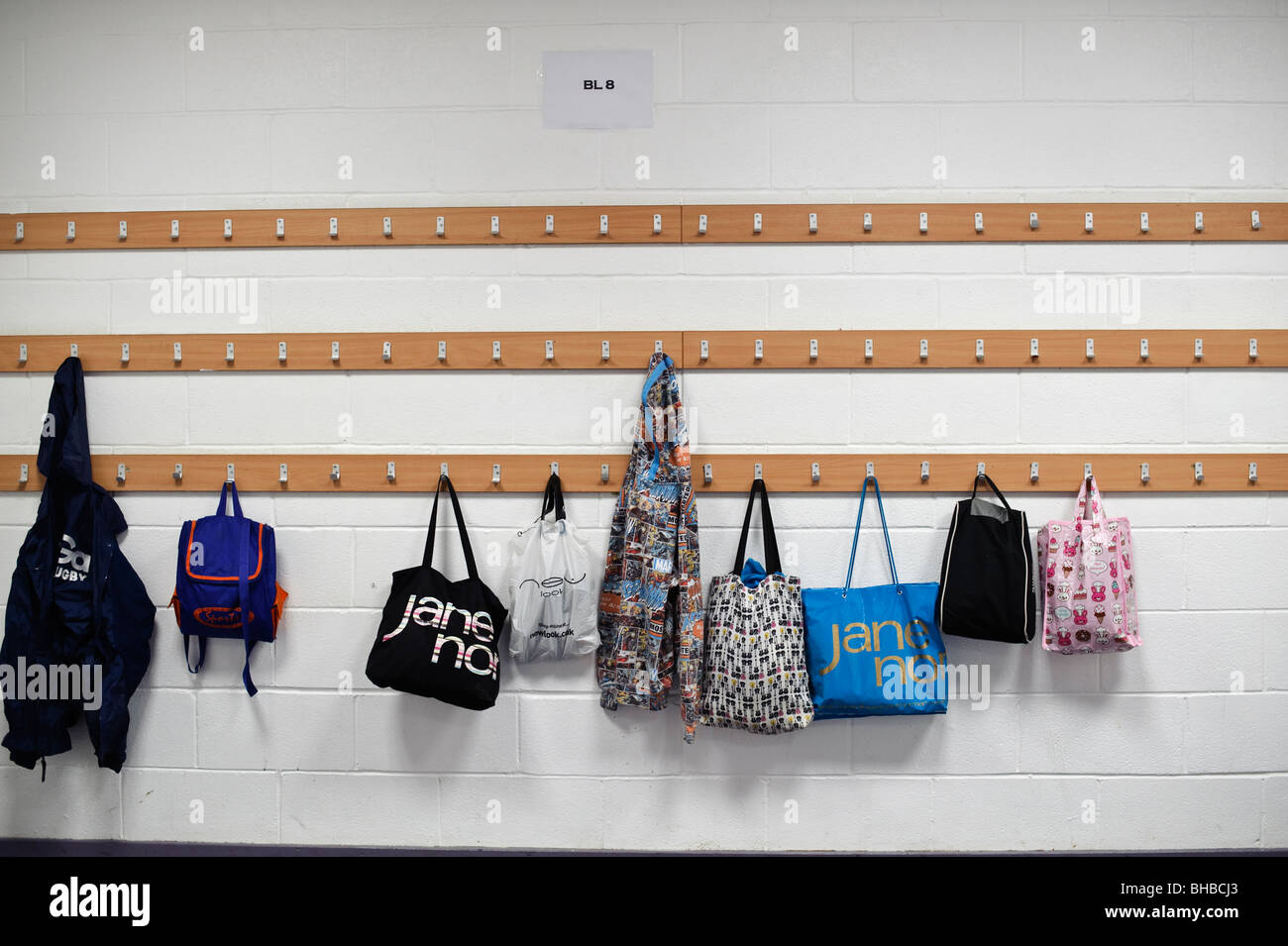 Bags hanging up on coat hooks in a secondary school cloakroom, UK Stock Photo
