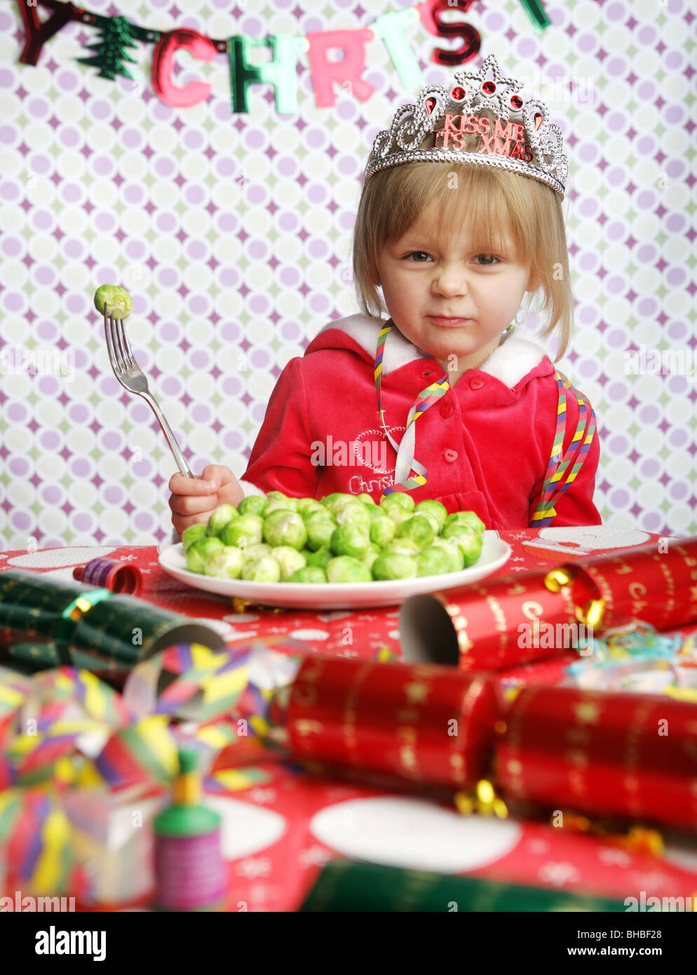 A young child sitting at a table decorated for Christmas with one sprout on her fork. Stock Photo