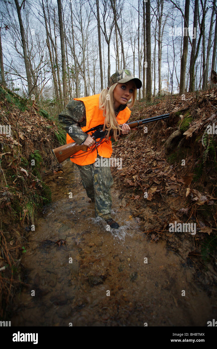 YOUNG WOMAN 21 Y.O. FEMALE DEER HUNTER MOVING QUICKLY THROUGH STREAM STALKING DEER  WATER SPLASHING MARLIN 30-30 CALIBER RIFLE Stock Photo