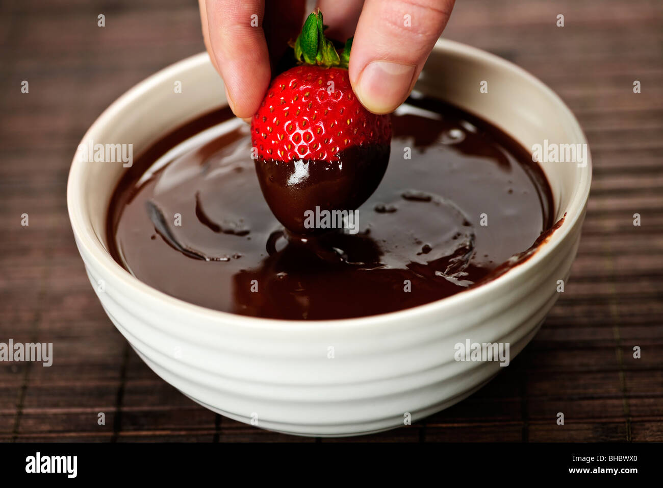 Hand dipping fresh strawberry in melted chocolate Stock Photo